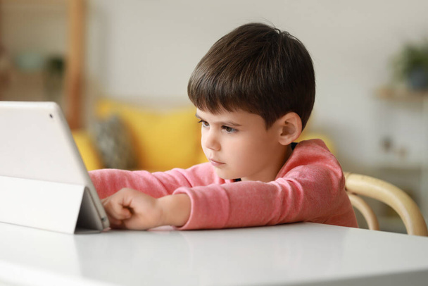 Маленький хлопчик дивиться мультфільми на планшетному комп'ютері за столом у вітальні
 - Фото, зображення
