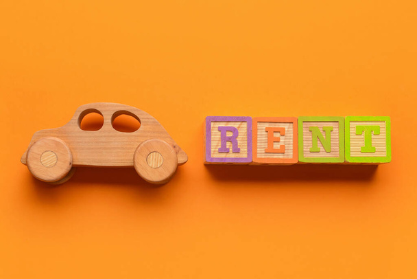 Ξύλινο αυτοκίνητο και λέξη RENT σε πορτοκαλί φόντο - Φωτογραφία, εικόνα