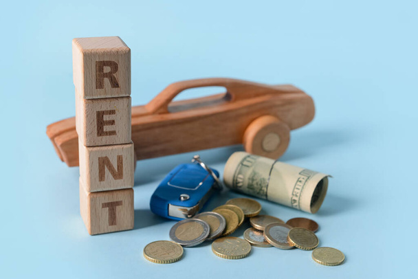 Houten auto met woord RENT, sleutel en geld op blauwe achtergrond - Foto, afbeelding