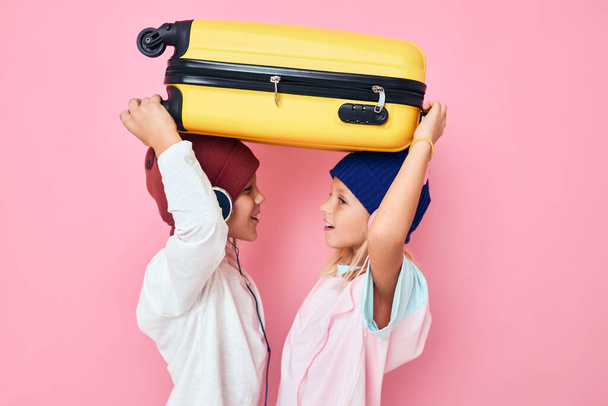 funny little boy and girl with a yellow suitcase in his hands pink color background - Photo, image