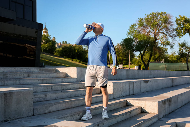 Sporty mature man drinking water on stairs outdoors - Photo, Image