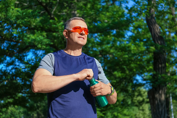 Sportieve volwassen man met fles water in het park - Foto, afbeelding