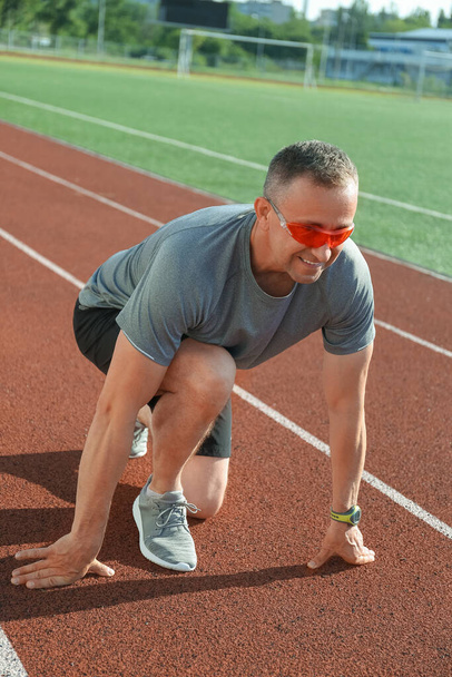 Urheilullinen kypsä mies valmistautuu juoksemaan stadionilla - Valokuva, kuva