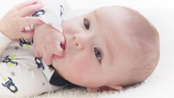 Bebé en el quinto mes de vida acostado y chupando los dedos de la mano. Fase oral de un bebé.  - Metraje, vídeo