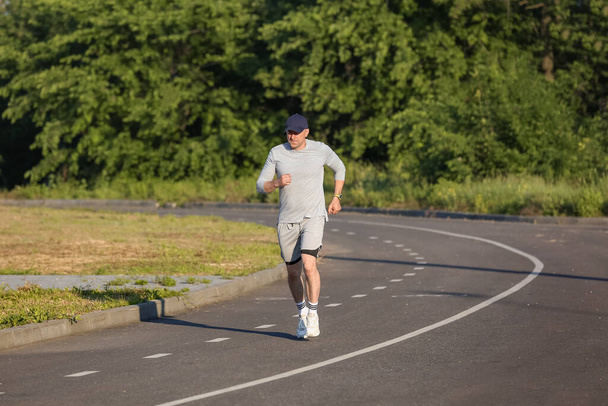 Sporty ώριμος άνθρωπος στο καπάκι τρέχει στο δρόμο - Φωτογραφία, εικόνα
