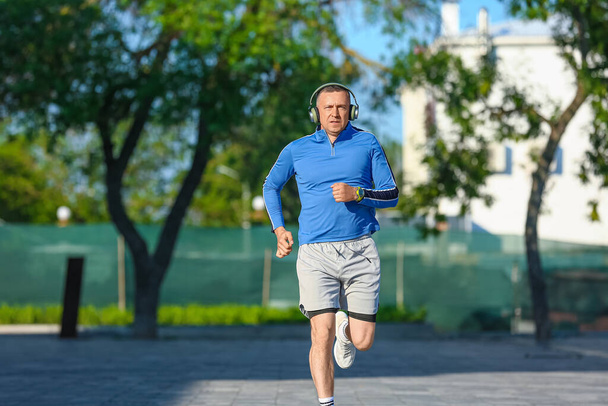 Deportivo hombre maduro con auriculares corriendo en el parque - Foto, Imagen