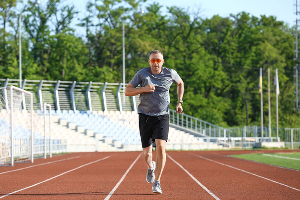 Sporty mature man jogging at stadium - Фото, изображение
