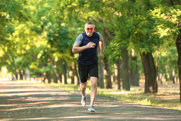 Sporty mature man with eyeglasses running in park - 写真・画像