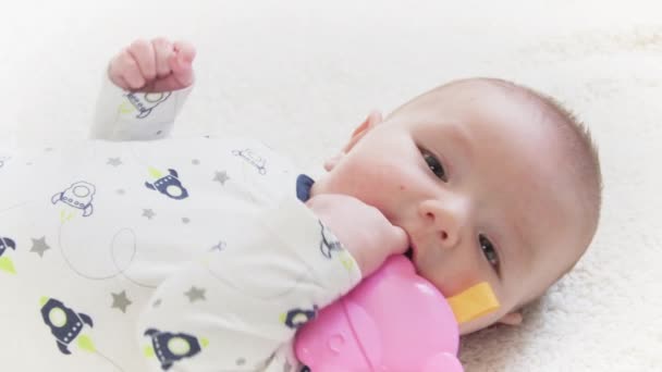 Bebê deitado no chão colocando seu brinquedo na boca. Desenvolvimento do bebê na fase oral. - Filmagem, Vídeo