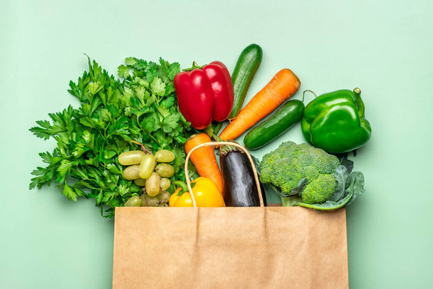 Экологически чистый бумажный магазинный пакет с сырыми органическими зелеными овощами, изолированными на зеленом фоне Плоская кладка, вид сверху на отходы, концепция без пластика - Фото, изображение