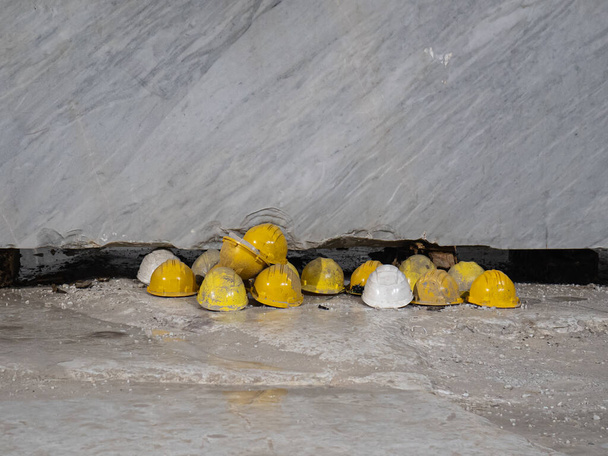 Capacetes de proteção de trabalho amarelo descansando no chão em frente a uma laje de mármore: trabalhadores da pedreira de mármore. - Foto, Imagem
