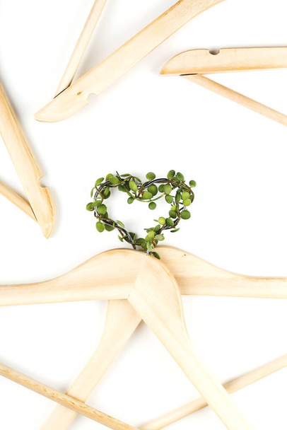 Conscious consumption slow fashion concept. Heart of clothes hangers entwined with green plant on white background.  - Photo, Image