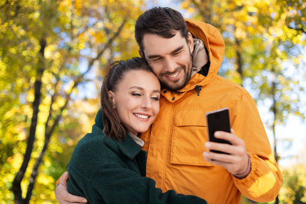 couple with smartphone over autumn park background - Photo, Image