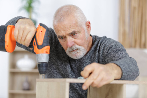 senior man is drilling a furniture - Фото, изображение