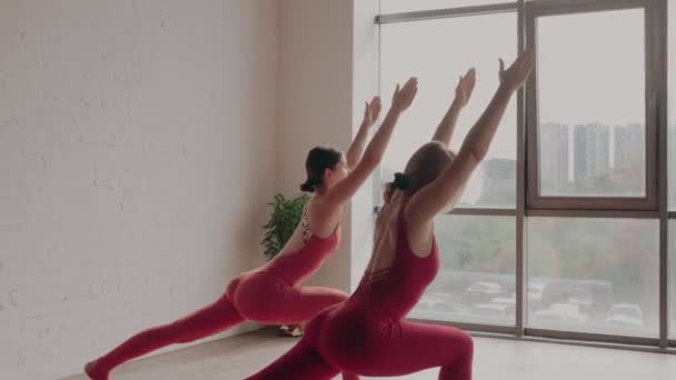 Deux femmes en uniforme de sport rouge font virabhadrasana en studio de yoga. Concept de mode de vie sain - Séquence, vidéo