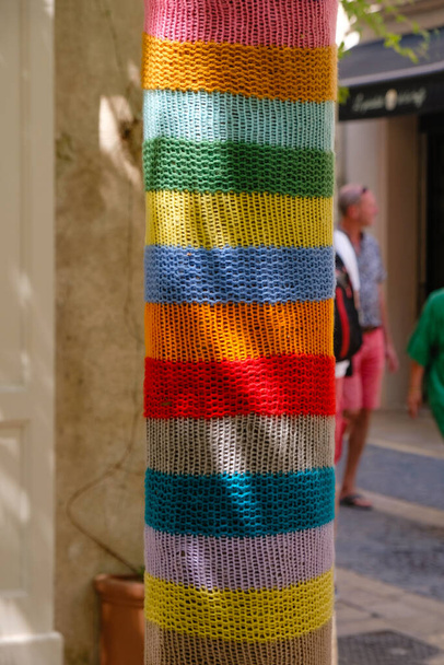 Rainbow yarn bombing in Saint-Remy-de-Provence, France. Colorful street art. Tourists in colorful clothes near the colored trees. Vertical image. - Photo, Image