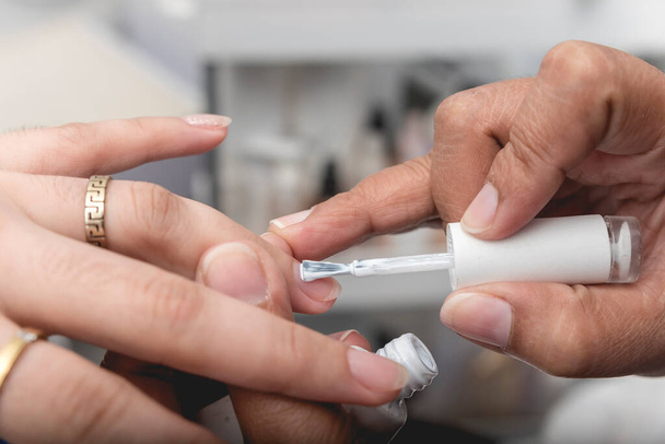 Manikérka nanáší bílý gel na prsteníček zákaznice. - Fotografie, Obrázek