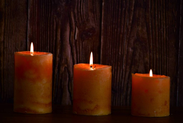 три восковых оранжевых свечи на деревянном фоне - Фото, изображение