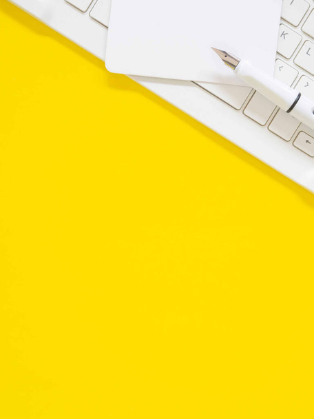 Επίπεδη lay, λευκή επαγγελματική κάρτα πάνω από το πληκτρολόγιο με στυλό σε ένα κίτρινο τραπέζι εργασίας. Κάτοψη με χώρο για κείμενο. Έννοια επιχειρήσεων και εκπαίδευσης.  - Φωτογραφία, εικόνα