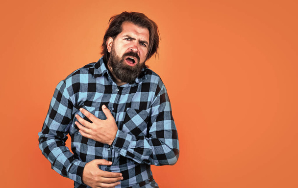 man has heartache on orange background. brutal bearded hipster feel pain. mature guy with moustache on face. expressing human emotions. suffering man in checkered shirt. copy space - Photo, Image