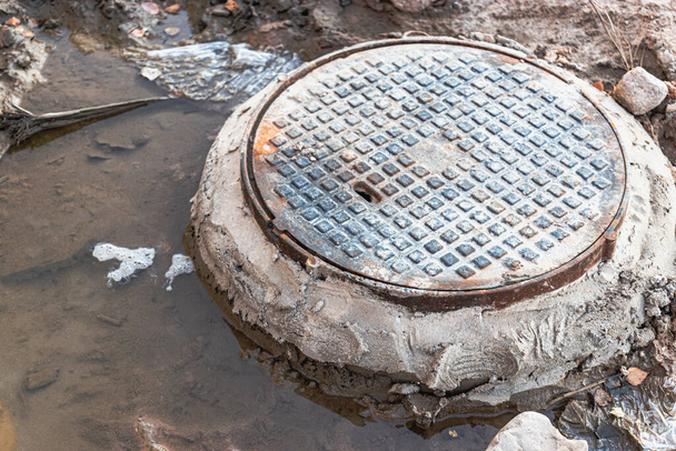 Um esgoto de ferro fundido cercado por uma poça de água num canteiro de obras. Construção de poços de esgoto - Foto, Imagem