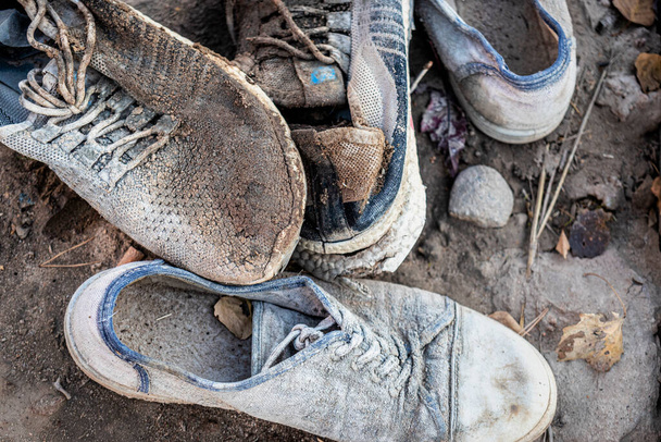 Stos starych brudnych butów leży na ziemi. Wykończone buty. Koncepcja ubóstwa i nędzy - Zdjęcie, obraz