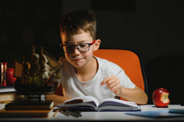 young teenager schoolboy at the table doing homework in the dark room - Φωτογραφία, εικόνα