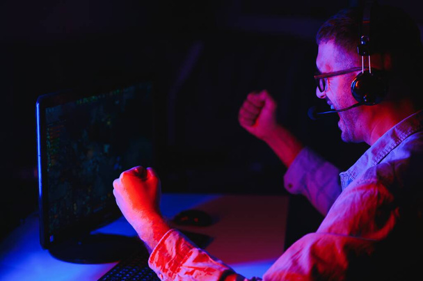 Professional Gamer Plays Video Game on His Computer. He's Participating in Online Cyber Games Tournament or in Internet Cafe. He Wears Glasses and Talks into Microphone. - Foto, Imagen