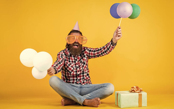 funny brutal bearded man wear checkered shirt having lush beard and moustache hold party balloons and present box, holiday - Photo, Image