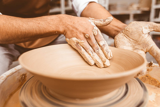 A young male potter works in his workshop on a potters wheel and makes clay products. Close-up of hands - Фото, изображение