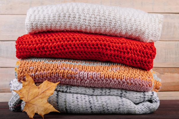Stack of warm knitted sweaters. Autumn concept. Woolen jumpers and maple leaf on a wooden background. - Photo, Image
