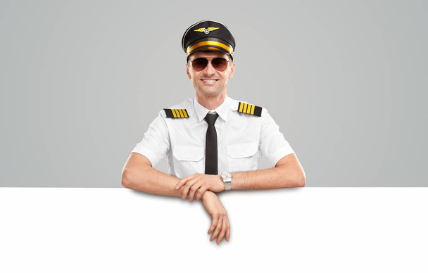 Cheerful aviator in uniform leaning on blank placard - 写真・画像