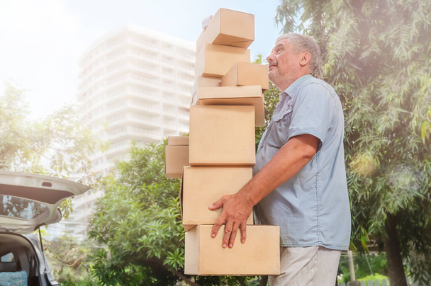 Senior man carries a high stack of cardboard boxes for moving in the car - Foto, immagini