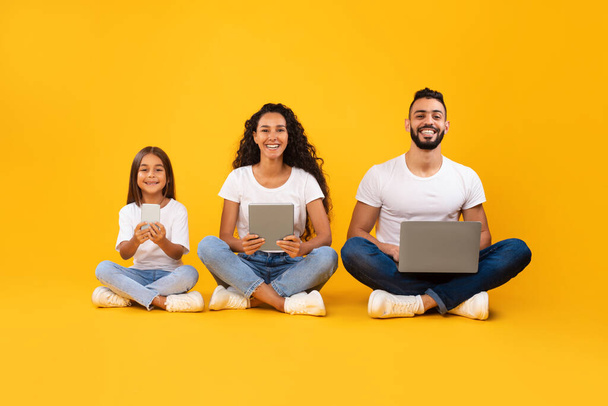 Arab Parents And Daughter Using Different Devices On Yellow Background - Photo, Image