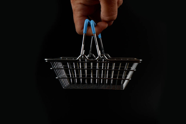 a small shopping basket hangs on a finger on a black background. - Foto, Imagen