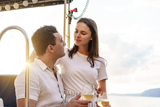 Young loving couple sitting on the yacht deck and drinking wine - Fotó, kép