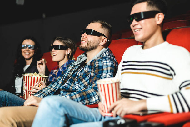 Friends are watching a movie in the cinema. People sit in the armchairs of the cinema and look at the screen with special glasses for 3D - Фото, изображение