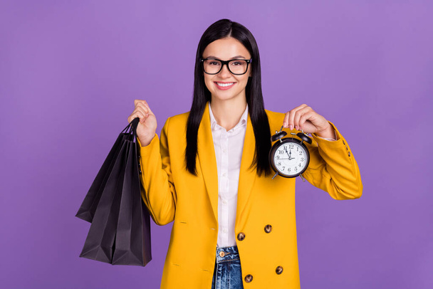Photo of pretty sweet young woman dressed yellow blazer spectacles holding bargains clock smiling isolated purple color background. - Фото, зображення