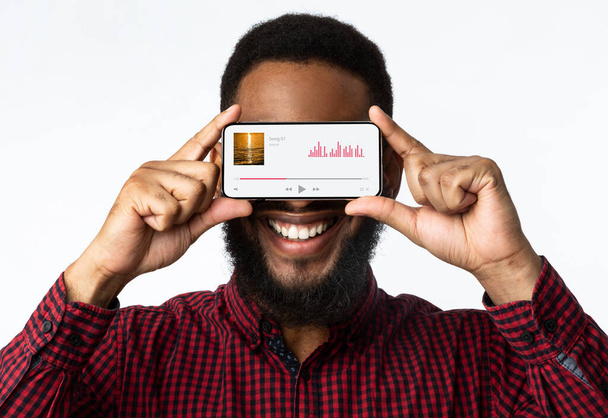 Музыкальный проигрыватель Веселый черный человек держа смартфон с аудио потоковое приложение - Фото, изображение