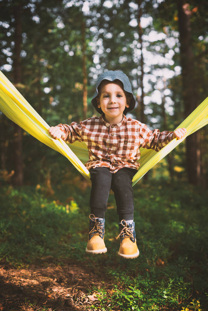 Small kid in yellow hammock in autumn forest - Foto, imagen