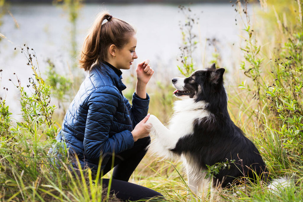 Cute girl in a blue jacket sits in front of her dog in the grass - Photo, Image