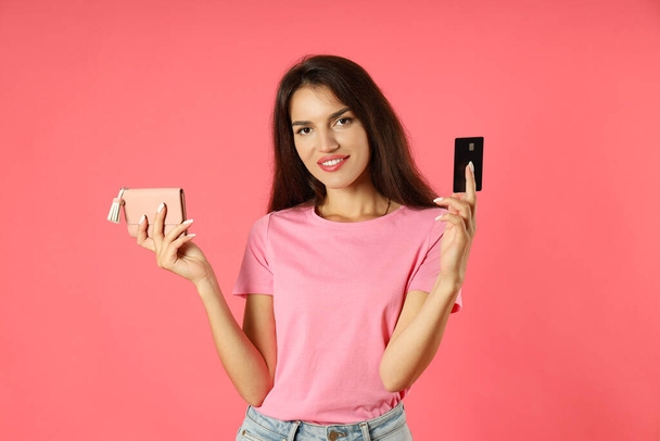 Ελκυστική κοπέλα κατέχει πιστωτική κάρτα και τσάντα σε ροζ φόντο. - Φωτογραφία, εικόνα