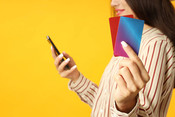 Attractive girl holds phone and credit cards on yellow background. - Foto, immagini