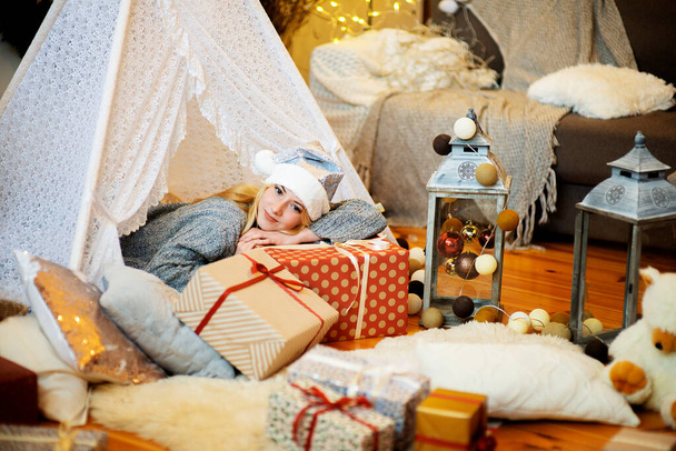 Csinos hölgy feküdt a karácsonyi ajándékdobozok visel kötött pulóver és Mikulás kalap díszített ünnepi otthon nappali - Fotó, kép
