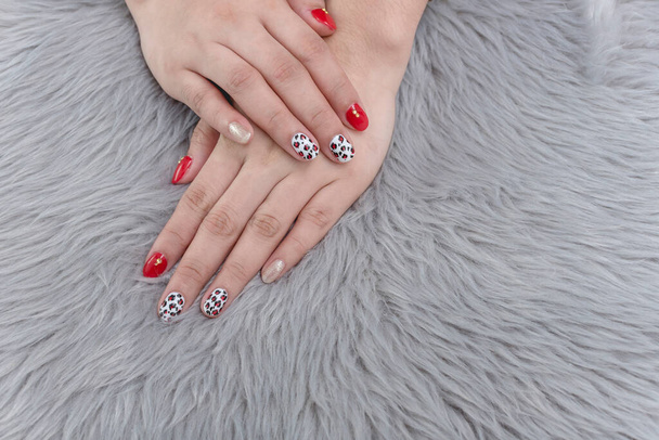 Two hands with a finish gel polished nails of mixed designs against a gray faux fur background. - Photo, Image