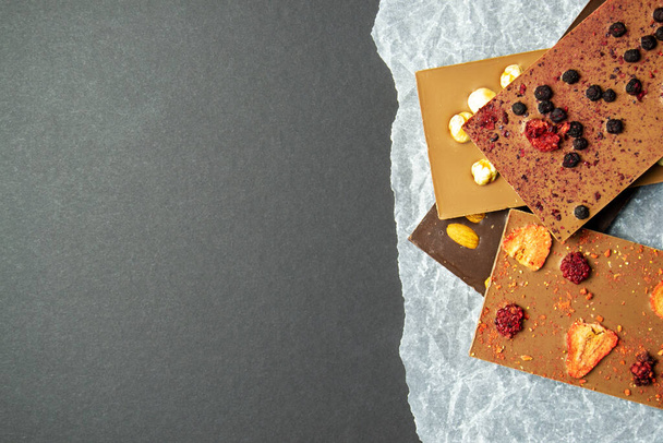 Batonik czekoladowy z migdałami, truskawkami, malinami, jagodami i orzechami laskowymi na papierowym tle. Słodycz z orzechami. czarne miejsce na wstawianie tekstu - Zdjęcie, obraz