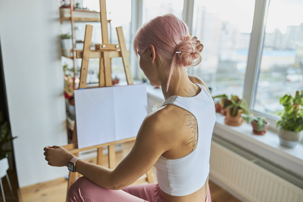 Elegante Künstlerin sitzt an Staffelei mit leerer weißer Leinwand auf zu Hause - Foto, Bild