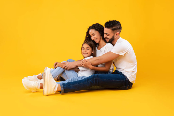 Side View Of Middle-Eastern Family Hugging Sitting Over Yellow Background - Photo, Image
