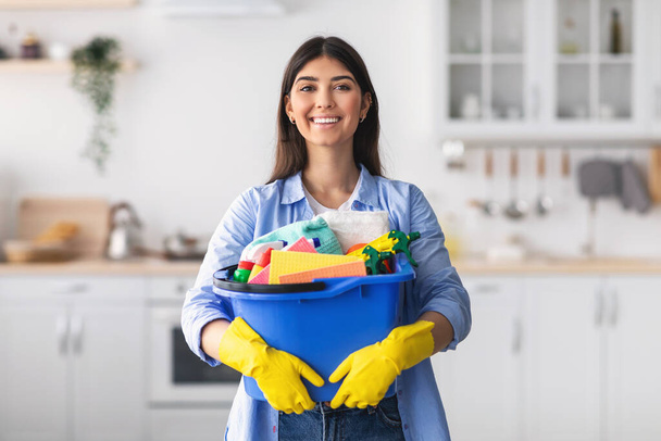 Genç ev hanımı elinde kovayla mutfakta temizlik malzemeleri tutuyor. - Fotoğraf, Görsel