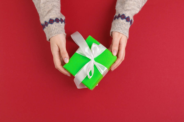 Female hands with christmas gift on red background, top view, copy space - 写真・画像